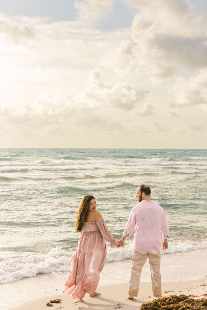 Couple walking by the ocean during a romantic maternity beach session in Miami.