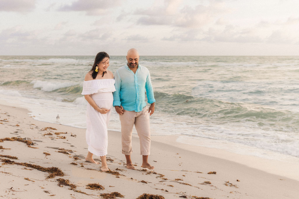 Maternity beach session couple walking along the shoreline in Miami during sunrise.