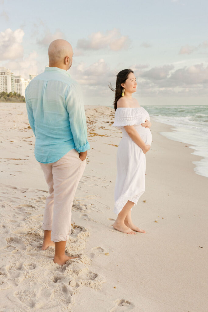 Maternity beach session couple walking barefoot along the shoreline in Miami.