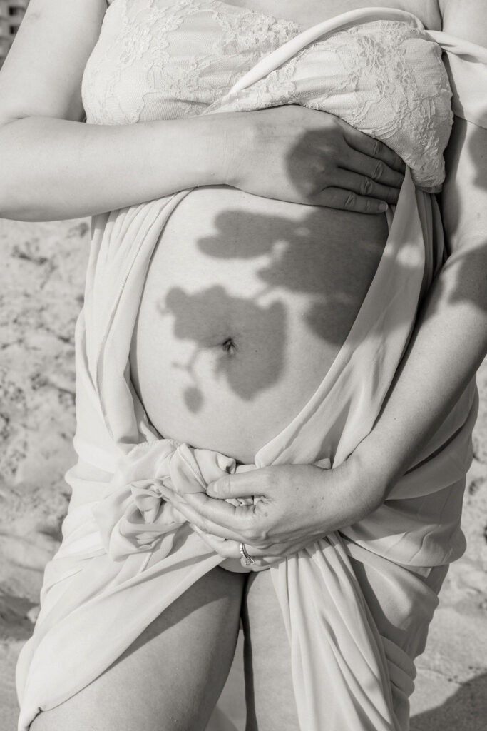 Artistic maternity beach portrait detail with floral shadow on baby bump.