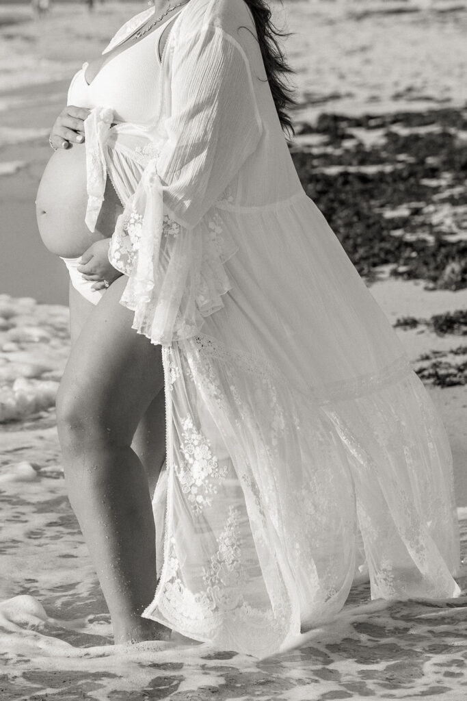 Black and white maternity beach photography portrait standing in ocean waves.