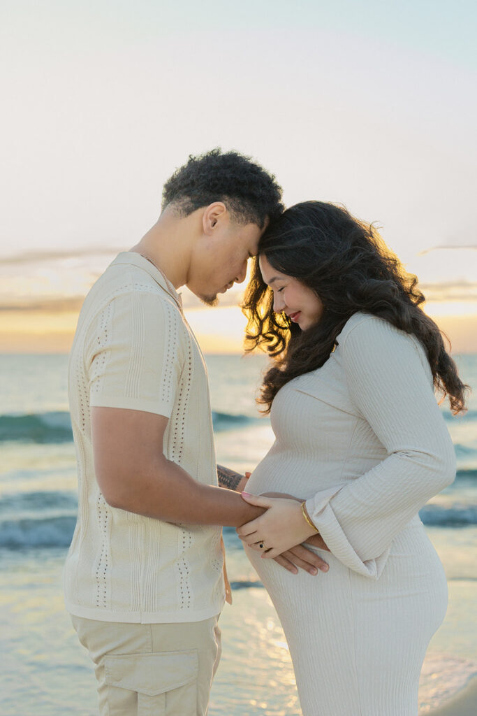 An intimate moment of an expecting couple during a beach session at golden hour.